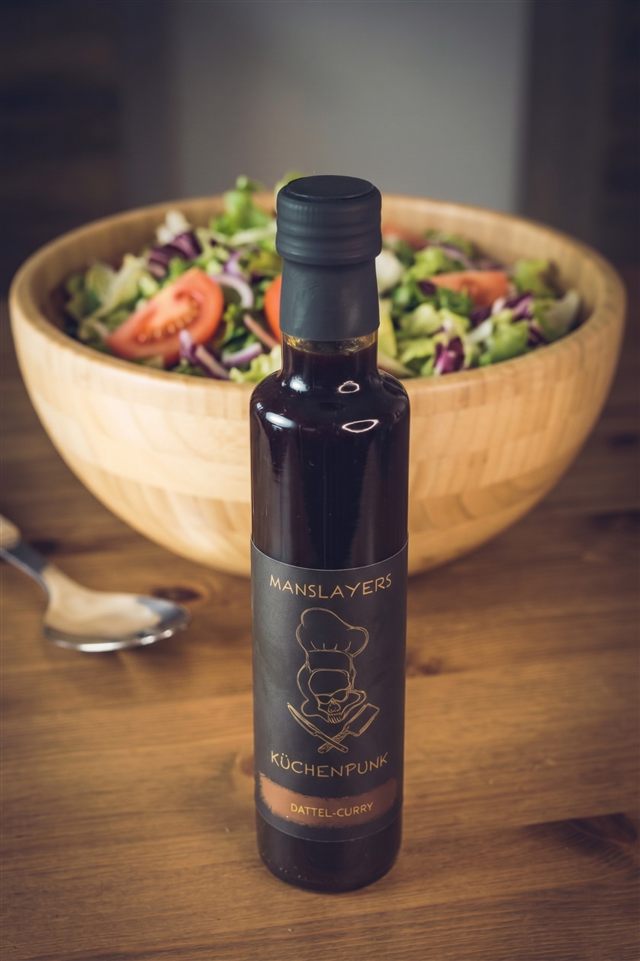 Manslayers Küchenpunk Dattel-Curry — dunkle Flasche vor einer Salatschüssel